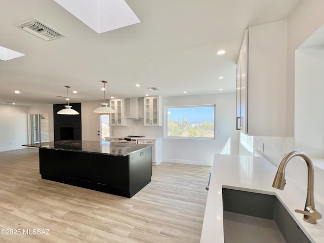 kitchen featuring a skylight, visible vents, wall chimney exhaust hood, stainless steel electric stove, and a sink