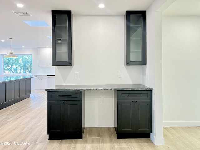 kitchen with glass insert cabinets, light wood finished floors, stone countertops, and visible vents