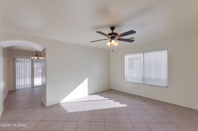 tiled empty room featuring ceiling fan with notable chandelier and a wealth of natural light