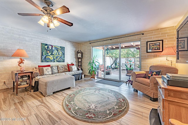 living room featuring ceiling fan, brick wall, and light wood-type flooring