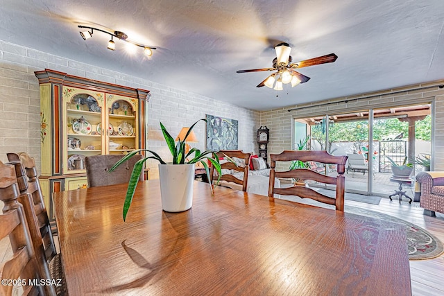 dining area featuring a textured ceiling, hardwood / wood-style flooring, ceiling fan, and brick wall