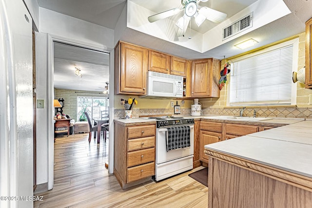 kitchen featuring white appliances, a raised ceiling, sink, light hardwood / wood-style flooring, and ceiling fan