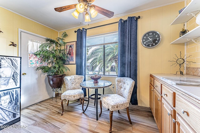 sitting room with light wood-type flooring, ceiling fan, and ornamental molding