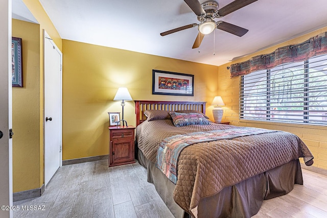 bedroom with light hardwood / wood-style flooring, ceiling fan, and brick wall