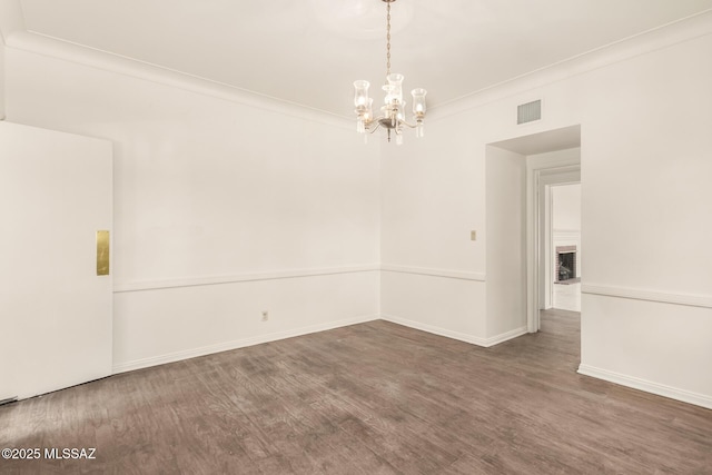 spare room featuring dark hardwood / wood-style flooring, an inviting chandelier, and crown molding