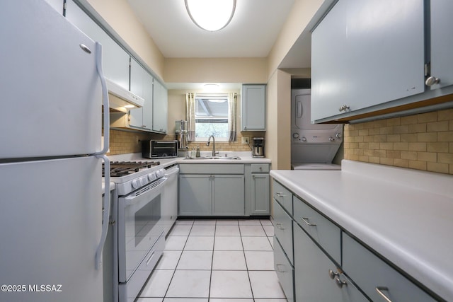 kitchen with stacked washer and dryer, sink, tasteful backsplash, light tile patterned floors, and white appliances