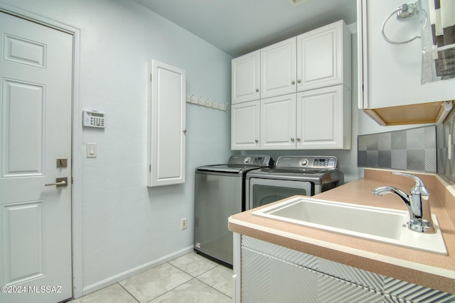 clothes washing area featuring light tile patterned floors, washing machine and dryer, a sink, baseboards, and cabinet space