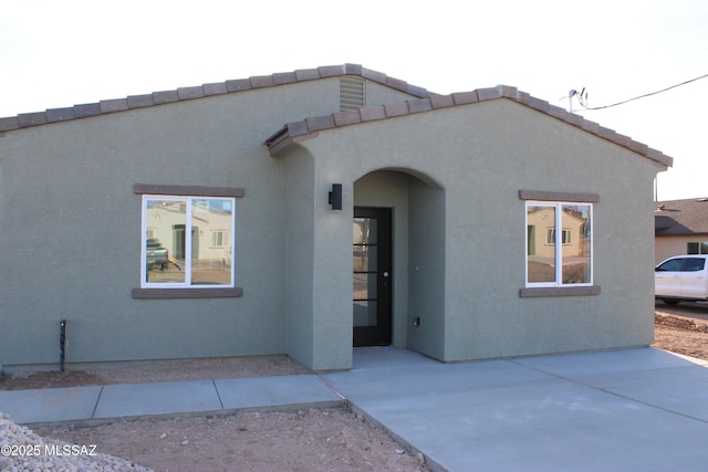 view of front of house with a tile roof, a patio, and stucco siding