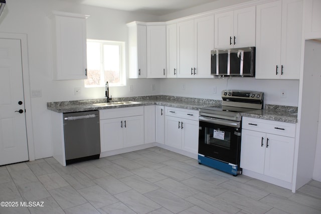 kitchen with a sink, stone counters, appliances with stainless steel finishes, and white cabinetry