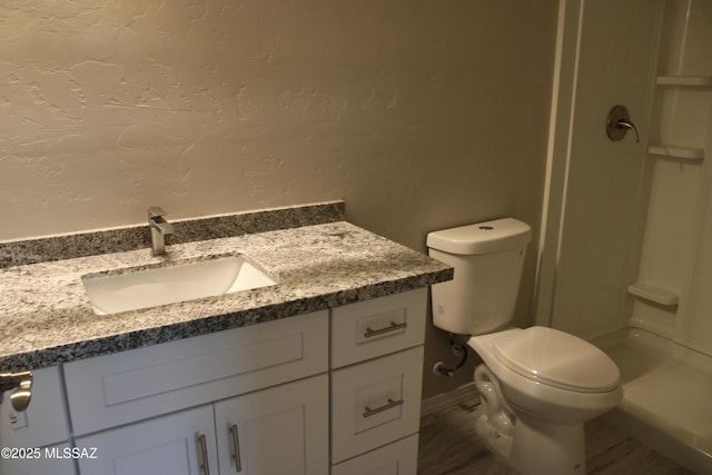 bathroom featuring toilet, a textured wall, a shower stall, and vanity