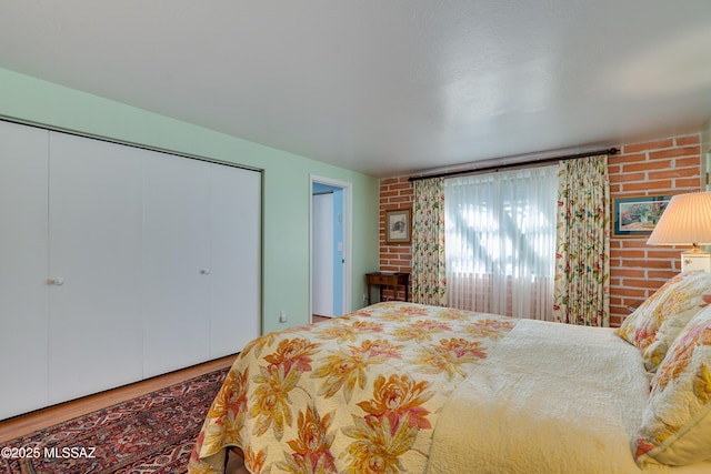 bedroom featuring multiple closets, brick wall, and wood-type flooring