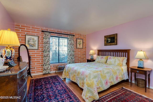 bedroom featuring brick wall and wood-type flooring