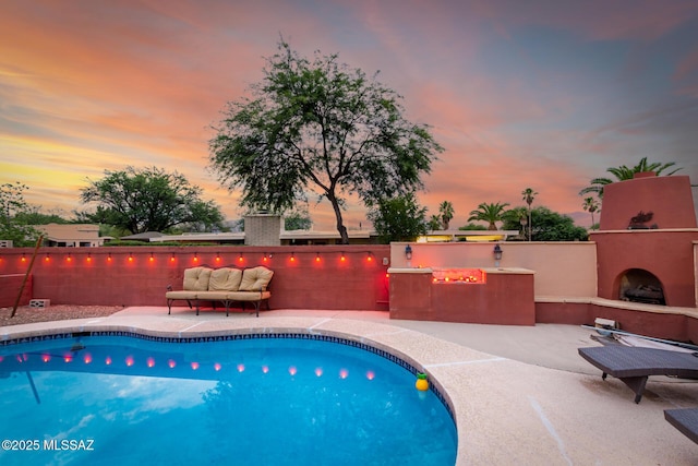 pool at dusk with a patio area and exterior fireplace