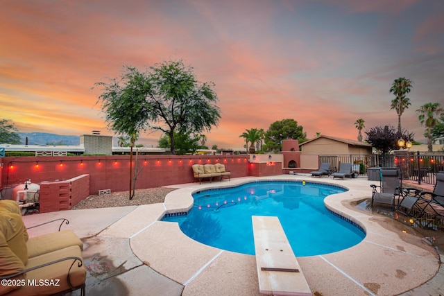 pool at dusk featuring a patio area and a diving board