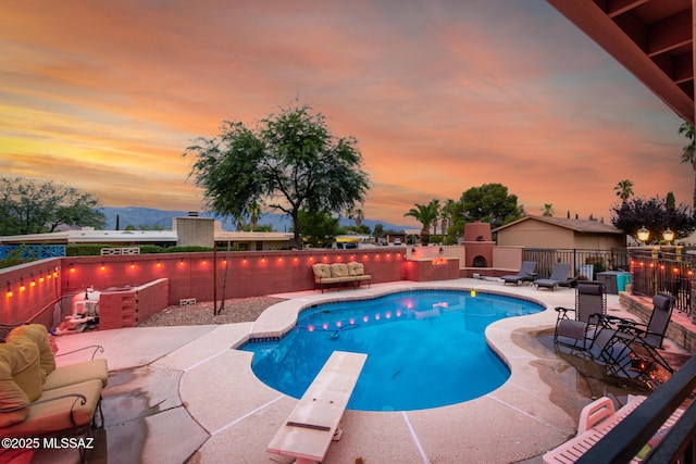 pool at dusk with a diving board, an outdoor fireplace, and a patio