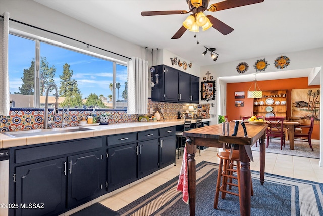 kitchen with backsplash, sink, decorative light fixtures, ceiling fan, and tile counters