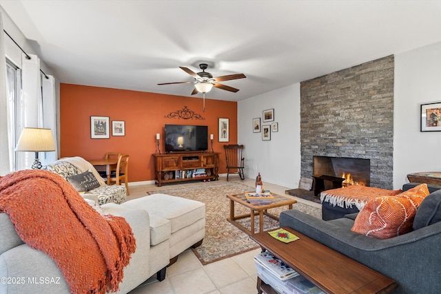 living room featuring ceiling fan, a stone fireplace, and light tile patterned floors