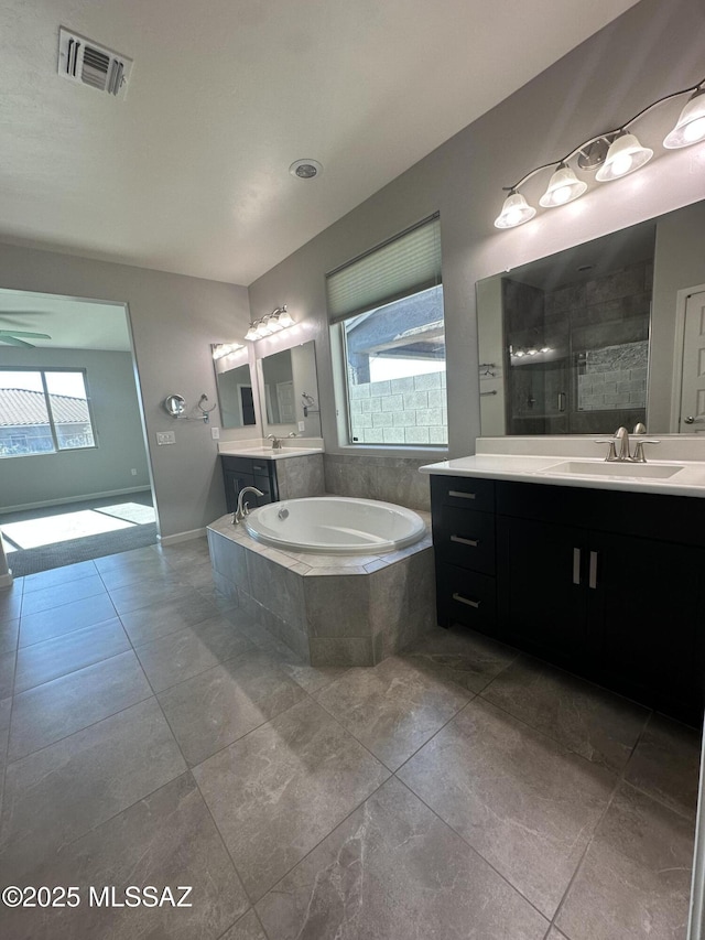 full bath featuring a bath, visible vents, tiled shower, two vanities, and a sink