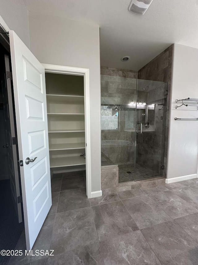 bathroom featuring visible vents, a walk in closet, baseboards, and a shower stall