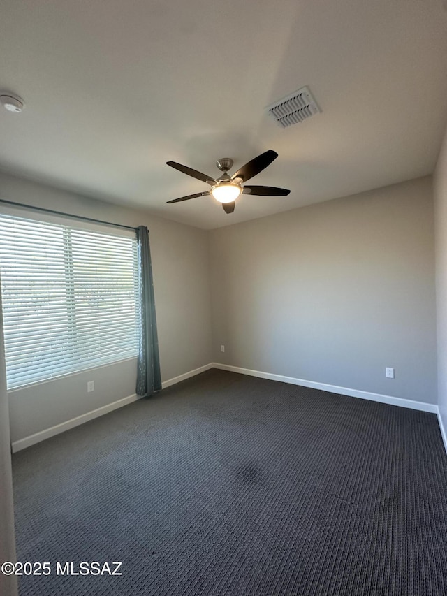unfurnished room with baseboards, dark carpet, ceiling fan, and visible vents