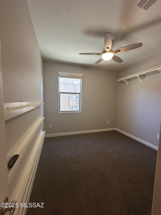 unfurnished room with baseboards, visible vents, dark carpet, and a ceiling fan