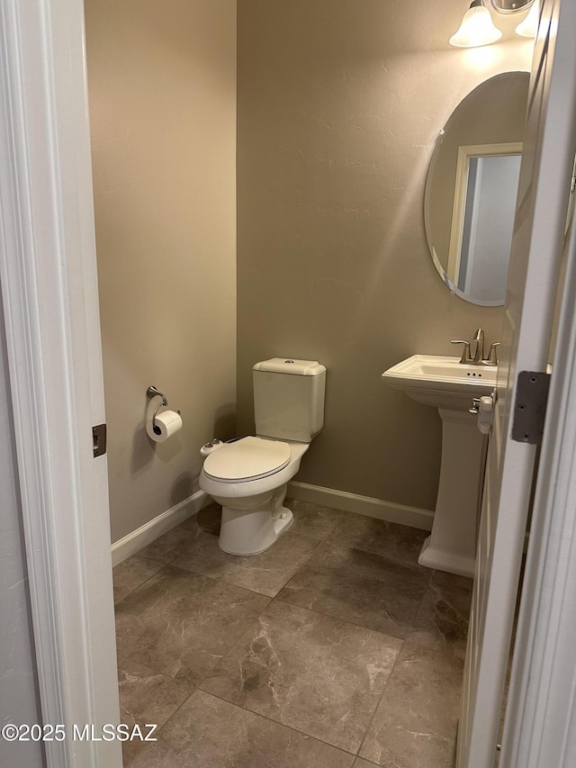 half bathroom featuring toilet, a sink, and baseboards