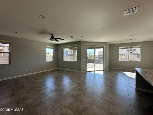 empty room with ceiling fan with notable chandelier, visible vents, dark tile patterned flooring, and baseboards