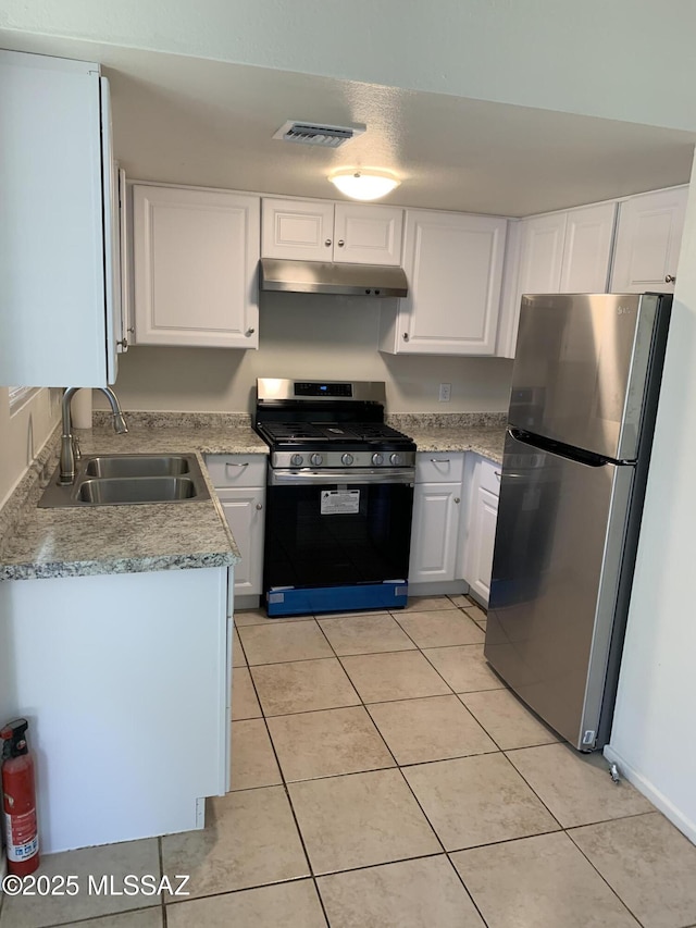 kitchen featuring sink, light tile patterned floors, gas range oven, white cabinetry, and stainless steel refrigerator