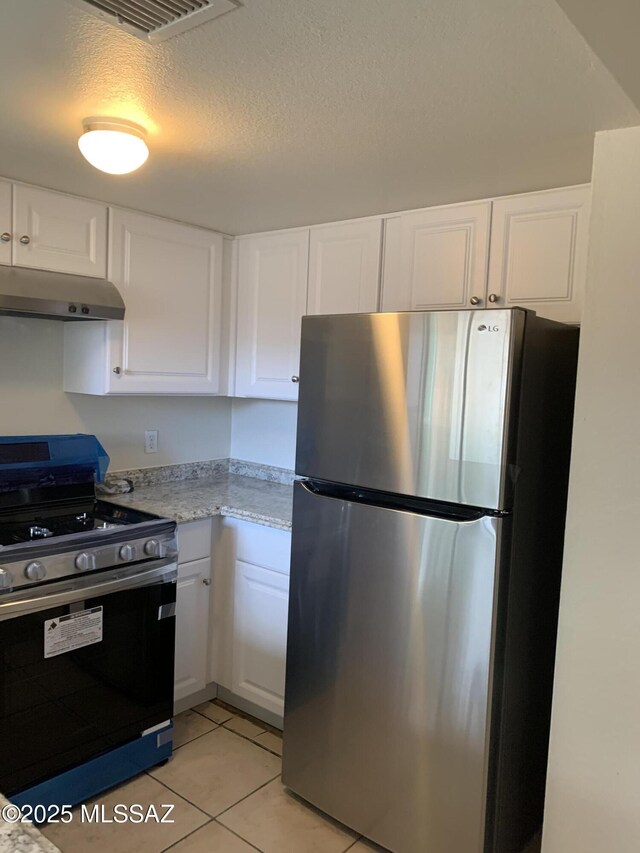 kitchen with white cabinets, black stove, light tile patterned floors, a textured ceiling, and stainless steel refrigerator