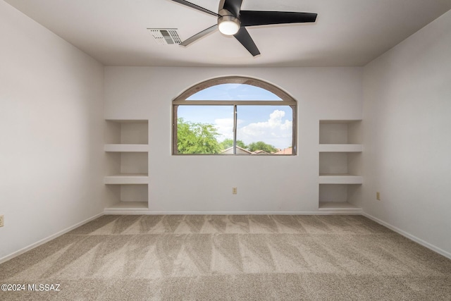 spare room featuring ceiling fan, built in features, and light carpet