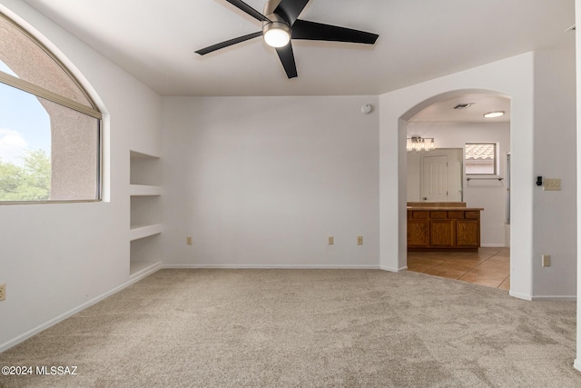 empty room with built in shelves, light colored carpet, and ceiling fan