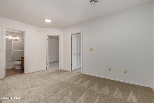 unfurnished bedroom with a spacious closet, light carpet, and connected bathroom