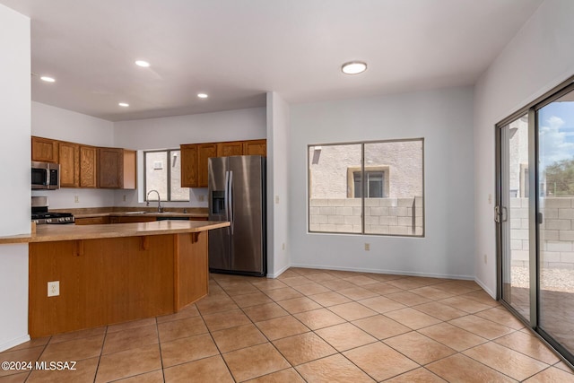 kitchen with a kitchen breakfast bar, light tile patterned floors, a wealth of natural light, kitchen peninsula, and stainless steel appliances