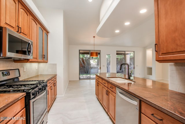 kitchen featuring tasteful backsplash, stainless steel appliances, sink, decorative light fixtures, and dark stone countertops