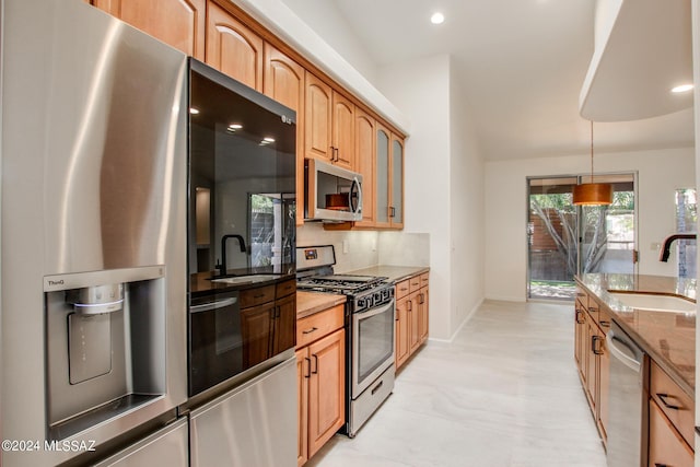 kitchen featuring appliances with stainless steel finishes, backsplash, light stone counters, sink, and decorative light fixtures