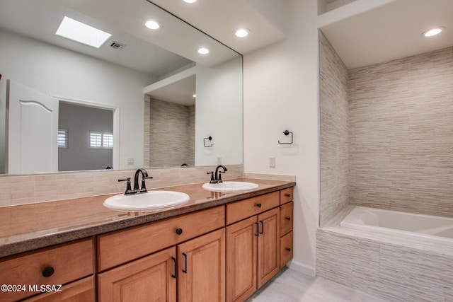 bathroom with vanity, a relaxing tiled tub, and a skylight