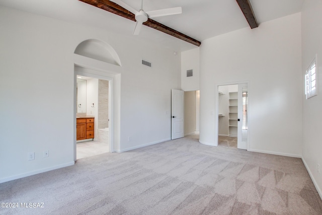 unfurnished bedroom featuring light carpet, ceiling fan, a spacious closet, beamed ceiling, and connected bathroom