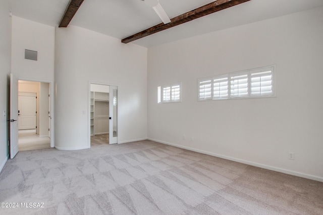 unfurnished bedroom featuring a walk in closet, light colored carpet, ceiling fan, beam ceiling, and a closet