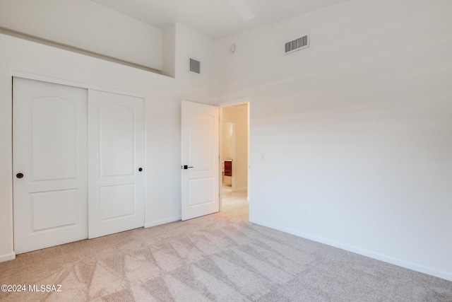 unfurnished bedroom with a high ceiling, light colored carpet, and a closet