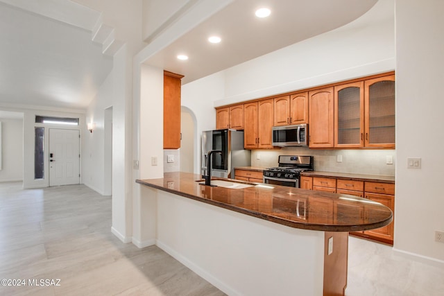 kitchen featuring sink, backsplash, kitchen peninsula, dark stone countertops, and appliances with stainless steel finishes