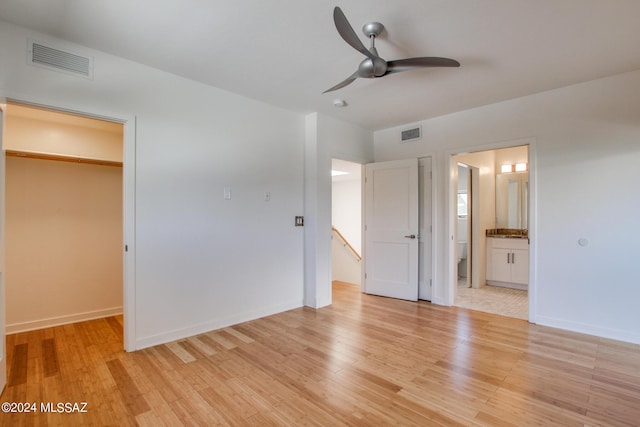 unfurnished bedroom featuring ensuite bath, ceiling fan, light wood-type flooring, a spacious closet, and a closet