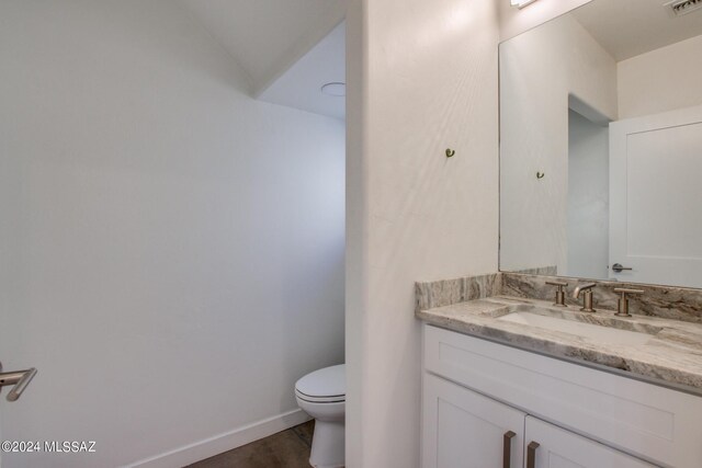 bathroom with hardwood / wood-style flooring, vanity, vaulted ceiling, and toilet