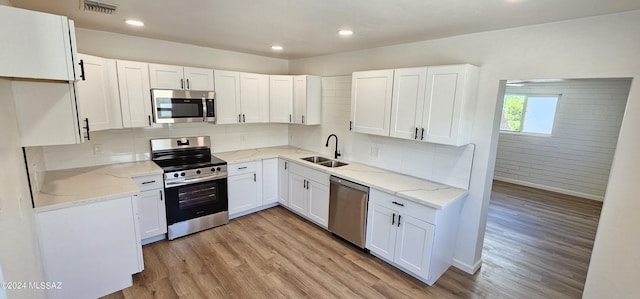 kitchen with appliances with stainless steel finishes, backsplash, sink, light hardwood / wood-style flooring, and white cabinets