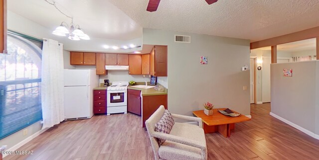 kitchen with light wood-type flooring, a textured ceiling, white appliances, sink, and hanging light fixtures