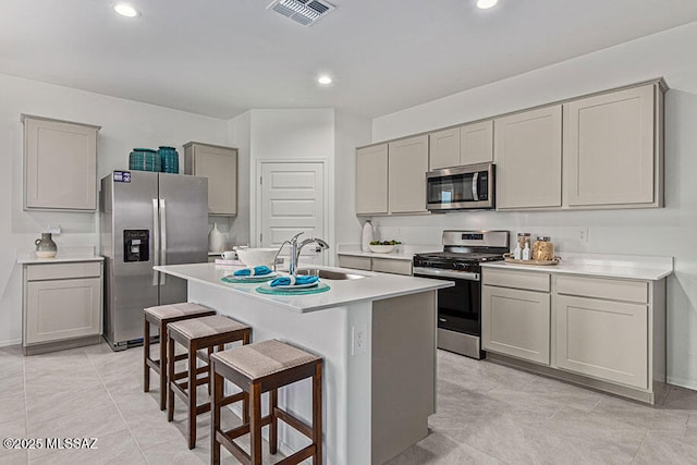 kitchen with gray cabinetry, a breakfast bar, stainless steel appliances, a kitchen island with sink, and sink