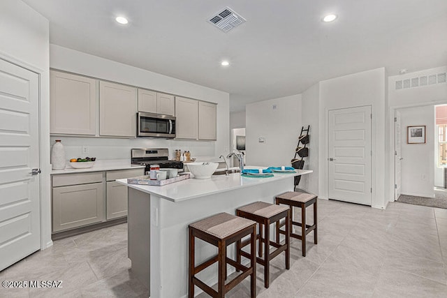 kitchen with a kitchen island with sink, sink, a breakfast bar area, gray cabinets, and stainless steel appliances