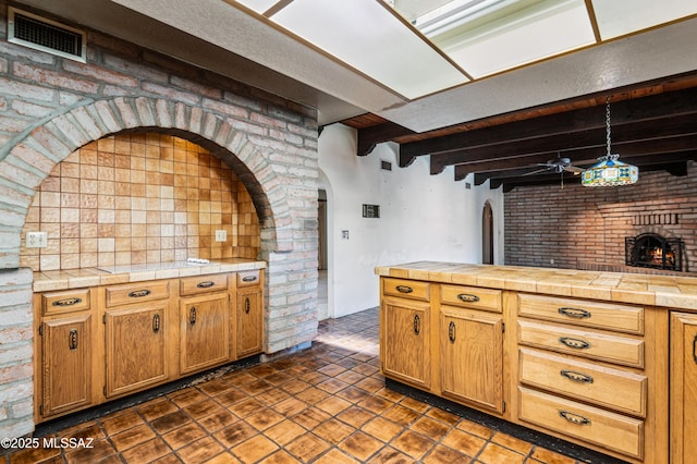 kitchen featuring a fireplace, beam ceiling, tile counters, and hanging light fixtures