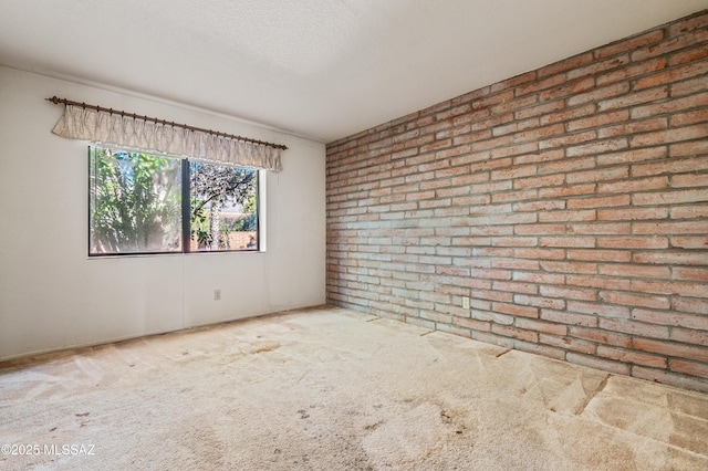 carpeted spare room featuring a textured ceiling and brick wall