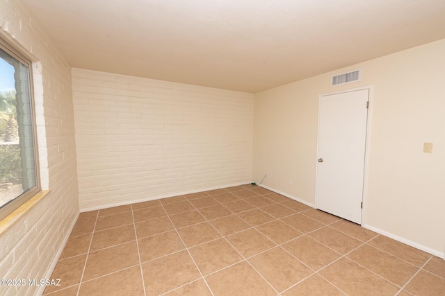 empty room with light tile patterned floors and brick wall