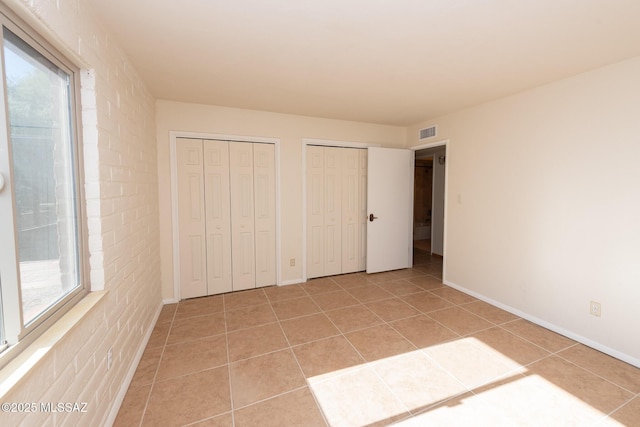 unfurnished bedroom featuring light tile patterned floors, two closets, and brick wall